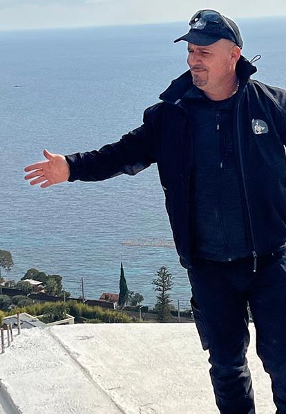 Patron Rina Étanchéité vérifie étanchéité toit, vue mer et montagnes derrière lui.